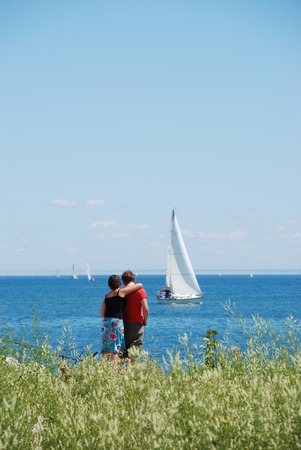 Couple on the shore looking at a sail boat on the horizon.の写真素材