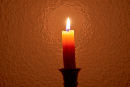 A close-up of a burning candle with a vibrant orange-toned background, evoking warmth, serenity, and a peaceful atmosphere.の写真素材