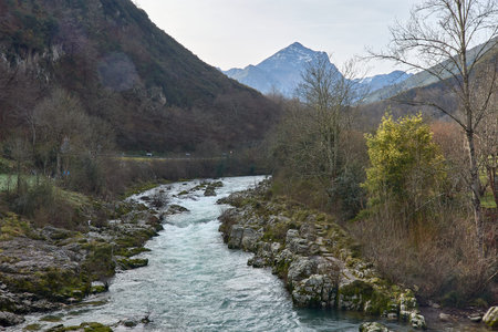 A scenic view of Rio Dobra flowing through a lush green forest along the hiking trail in Asturias,...
