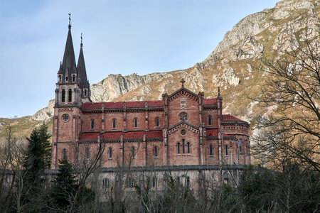 The Basilica of Santa Maria in Covadonga, Asturias, Spain, is a stunning neo-Romanesque church surrounded by breathtaking mountains. This iconic religious site is a major pilgrimage destination and a symbol of Asturian history and culture. Its red stone faÃ§ade and twin bell towers stand out against the natural landscape, creating a spectacular view.の写真素材