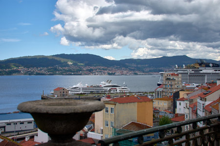 Overlooking the Ria de Vigo from the Paseo de Alfonso XII, this image captures the expansive view of the waterway, distant hills, and the cityscape. The tranquil blue waters reflect the sky, with boats dotting the horizon. Buildings line the shore, showcasing the urban landscape against the natural beauty of the Galician coastline.の写真素材