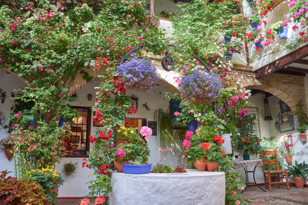 Traditional Andalusian patio filled with pots of brightly colored flowers such as geraniums, petunias, and bougainvilleas, decorating whitewashed walls and a central well. A harmonious composition with natural light, handcrafted elements, and lush vegetation, ideal for representing cultural tourism, spring, and the Mediterranean lifestyle.の写真素材