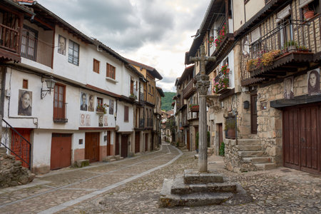 an evocative cobblestone alley in the village of Mogarraz, Salamanca, flanked by traditional houses with wooden balconies and stone walls. A distinctive element is the photographic portraits of residents adorning the facades, a project that pays homage to the town's identity and history. The linear composition guides the eye through the street, revealing the unique fusion of architectural heritage and cultural expression, ideal for publications on rural tourism, urban art, local history, or the authenticity of Spanish villagesの写真素材