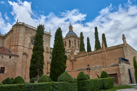 Partial view of Ciudad Rodrigo Cathedral in Salamanca, with its Romanesque-style tower standing out among green treetops under a cloudy sky. The warm tones of the stone contrast with the gray and blue of the sky, creating a solemn and serene atmosphere. Ideal image for editorial projects, travel guides, cultural and historical tourism.の写真素材