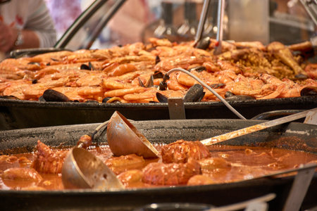 A freshly cooked rice dish It is presented in the foreground on a metal tray at an open-air market in Aix-en-Provence. The warm tones of the rice contrast with the blurred background of utensils and a street atmosphere, conveying authenticity, flavor, and tradition. Ideal for editorial, gastronomic, or culinary tourism promotionsの写真素材