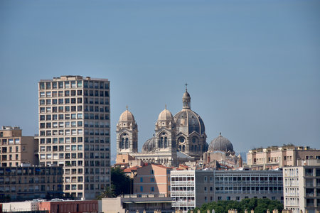 From an elevated perspective, the Port of Marseille unfolds, filled with sailboats and yachts, framed by the Old Town waterfront and the city's historic architecture. The blue tones of the sky and sea contrast with the warm colors of the buildings, while the traffic and vegetation add dynamism and urban life. This image is ideal for tourism projects, Mediterranean destination promotion, urban planning, and coastal lifestyle projects.の写真素材