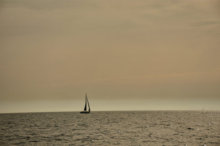 A white-sailed sailboat sails in the foreground through the crystal-clear waters of the French...