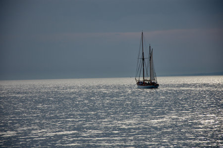 A sailboat sails in the foreground through the crystal-clear waters, while other boats and sailboats...