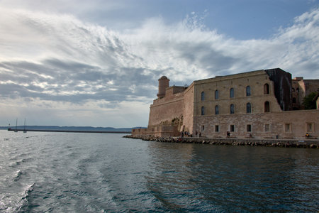 From the perspective of a boat, the iconic Port of Marseille is filled with yachts and sailboats, framed by the city's historic architecture and a deep blue sky. The composition conveys serenity and evokes the Mediterranean atmosphere, highlighting the harmony between the sea, the boats, and the city. The predominant colors are the blues of the water and sky, along with the warm tones of the buildings, ideal for illustrating concepts of tourism, travel, and coastal lifestyleの写真素材