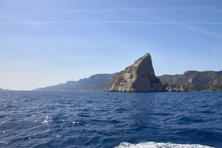 From the stern of a moving boat, the imposing rocky silhouette of the Calanques of Marseille can be...