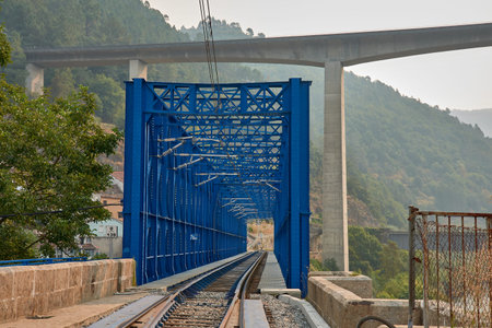 A railway bridge with blue-painted iron frames the railway track in a symmetrical and deep...