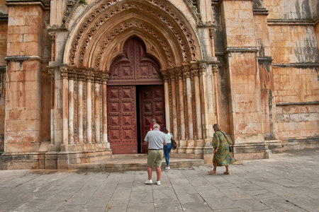 Several visitors are seen entering through the impressive Gothic-style main gate of the Batalha...