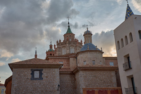 The tower of the Cathedral of Santa Maria de Mediavilla in Teruel rises in the Mudejar style with red brick, ornamental windows, and a green dome crowned by a metal cross. The blue sky highlights the texture of the materials and conveys serenity. Ideal for editorial, tourism, and cultural projects related to historical heritage and religious architectureの写真素材