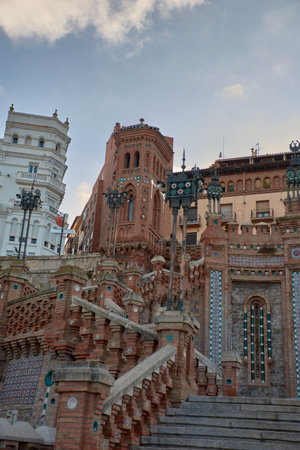 The majestic Oval Steps in Teruel are an impressive Neo-Mudejar monumental complex, characterized by their wide stone staircases that ascend to the upper part of the city. Flanked by two reddish brick towers with domes and tiled decorations, the steps include a large sculptural relief depicting a biblical passage and a semicircular fountain at the base, all set against a sky with dramatic clouds that enhance the grandeur of the complex. This work, which connects the lower city with the station, is ideal for illustrating themes of heritage, architecture, public art, tourism in Spain, history, urban life, and the beauty of historic buildings.の写真素材