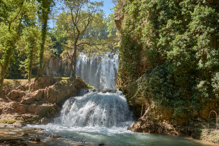 Waterfalls of the Cistercian Monastery of Piedra Natural Park in Aragon, Spain, with water flowing vigorously between moss-covered rocks and lush vegetation. Sunlight illuminates the water droplets, creating reflections and sparkles that enhance the freshness and dynamism of the natural environment. They are ideal for projects on tourism, nature, ecology, hiking, wellness, or any theme that seeks to convey the beauty and power of water in idyllic landscapesの写真素材