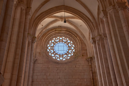 The interior of the Monastery of Alcobaca reveals a vault A raised Gothic ceiling with ribs converging over a blue rose window with geometric tracery. Natural light highlights the symmetry of the columns and the texture of the stone, creating a solemn and spiritual atmosphere. Ideal for representing sacred architecture, medieval heritage, and cultural tourism in Portugalの写真素材