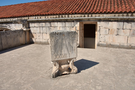 A carved stone sundial stands on a decorative pedestal on a terrace of the Alcobaca Monastery, with engraved Roman numerals and a shadow cast by the gnomon. The architectural background and clear sky add depth and serenity to the scene. Ideal for depicting historical heritage, ancient methods of timekeeping, and Portuguese sacred architectureの写真素材