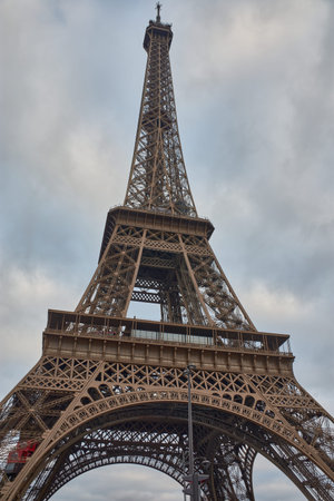 The Eiffel Tower rises imposingly in Paris under a cloudy sky, highlighting its wrought iron...