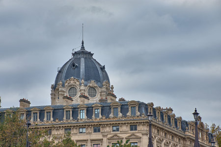 The dome of the Registry of the Commercial Court of Paris rises elegantly above a stone facade decorated with reliefs, arched windows, and classical sculptures. The dark slate roof contrasts with the gray sky, creating a sovereign and monumental atmosphere. Ideal for illustrating topics of institutional architecture, urban heritage, and classic French designの写真素材