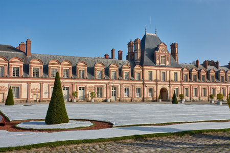 One of the facades of the Palace of Fontainebleau is presented with symmetry and elegance, framed by covered gardens to protect the lawn from the cold. The blue sky and natural light enhance the warm tones of the stone and the geometry of the landscape. Ideal for illustrating topics of heritage conservation, historical architecture, and royal garden managementの写真素材