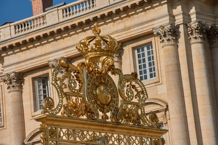 The Golden Gate of the Palace of Versailles features an ornamental structure of gilded wrought iron, crowned by a large decorative crown and a central coat of arms with the fleur-de-lis. The architectural background with classical columns and a clear sky reinforces the solemn and symbolic character of the complex. Ideal for tourism, historical content, and editorial content on French heritage and decorative artの写真素材