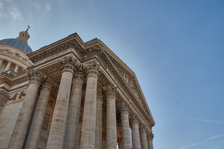 The Pantheon of Paris stands majestically in the Latin Quarter, distinguished by its neoclassical facade with Corinthian columns, sculpted pediment, and central dome crowned by a cross. Natural light highlights the architectural details against the blue sky, evoking the legacy of great French figures. Ideal for tourism, editorial, and cultural content on national history, monumental architecture, and European heritageの写真素材