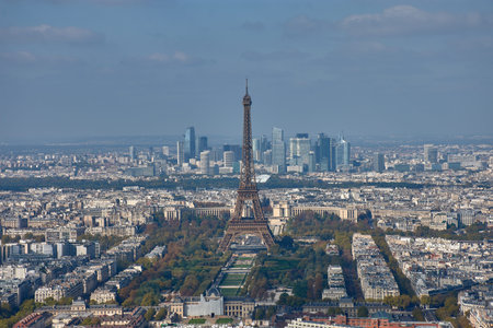 From the top of the Montparnasse Tower, a panoramic view of Paris unfolds, with the Eiffel Tower majestically centered in the frame. In the background, the skyscrapers of the La Defense district contrast with the classic architecture of the historic center, creating a visual composition that reflects the duality between tradition and modernity. Ideal for tourism, editorial, and cultural content related to urban planning, Parisian heritage, and travel photographyの写真素材