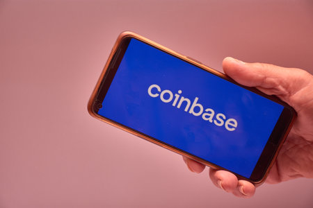 Vigo, Spain, November 30, 2025.A human hand holds a smartphone whose screen displays the logo of Coinbase, a US-based cryptocurrency trading and investment platform. The clean, corporate blue background reinforces the brand's visual identity and conveys tのeditorial素材