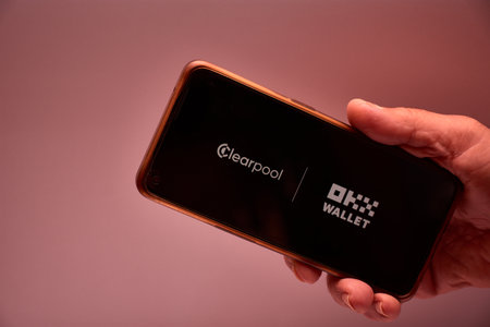 Vigo, Spain, November 30, 2025.A human hand The image features a smartphone displaying the OKX logo, a centralized exchange and wallet platform based in Seychelles. The black background and geometric design reinforce the technological and corporate aestheのeditorial素材