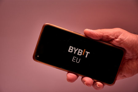 Vigo, Spain, November 30, 2025.A human hand holds a smartphone whose screen displays the logo of Bybit, a Singapore-based centralized exchange specializing in cryptocurrency derivatives. The black background and minimalist design reinforce the technologicのeditorial素材