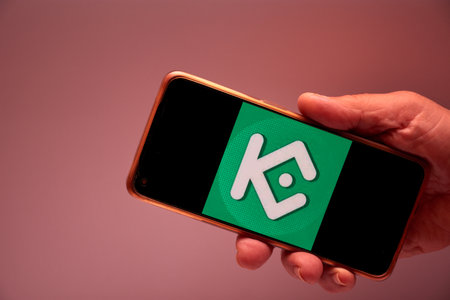Vigo, Spain, November 30, 2025.A human hand holds a smartphone whose screen displays the KuCoin logo, a cryptocurrency exchange platform focused on security, accessibility, and intuitive design. The green background reinforces the brand's visual identity のeditorial素材