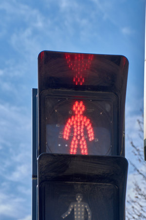 A pedestrian traffic light displays the silhouette of a man standing still, illuminated in bright...