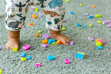 Baby legs on a grey carpet and toy bricks are around.