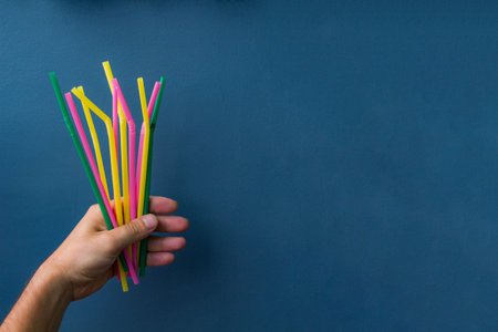 Close up of hand holding plastic colourful straws on blue background