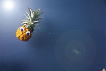 Fresh pineapple with googly eyes looks like flying, hang on air on blue background, enough place for text. Good concept for magic.の写真素材