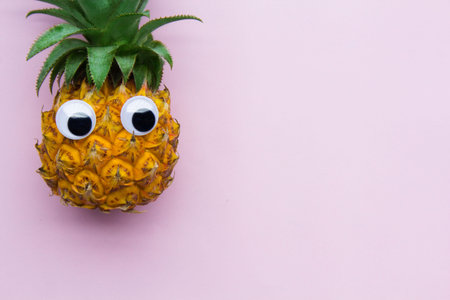 Fresh funny pineapple with googly eyes on pink background, enough place for text. .の写真素材