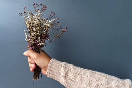 Man in warm brown sweater hold dried flowers on blue background