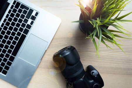 Photographer lay camera on wooden table near green flower, modern laptop. Closeup of working place of creative person.の写真素材