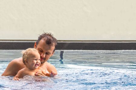 Cute baby swims with the father in a swimming pool in sunny summer day. There is a place for you text.の写真素材
