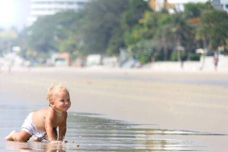 baby plays in water on a sea shore in a sunny weater in summerの写真素材