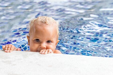 Cute baby swims in a swimming pool in sunny summer dayの写真素材