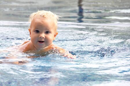 Cute baby swims in a swimming pool in sunny summer dayの写真素材
