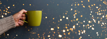 Man in a warm winter brown sweater keeps a green mug in his right hand in gray background. Good...