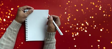 Mans right hand holds white pen and left hand holds a white papered blank notebook, view from the top, red background, bannerの写真素材