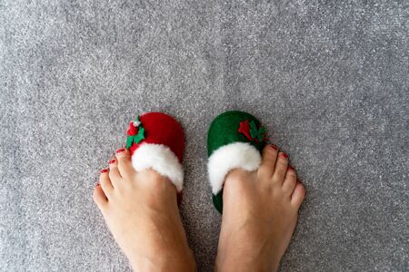 Legs in Christmas red and green slippers are on grey rug, view from the top, new year conceptの写真素材