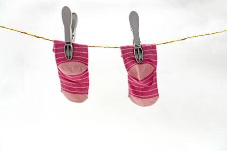 Pink little baby socks hang at clothesline with the help of grey clothespin on white background, isolated.の写真素材