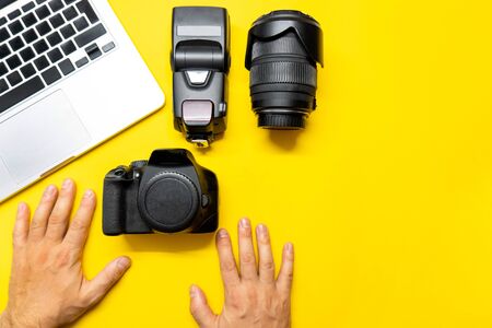 Photo camera and other accessories such as flash light and lens are on the table near laptop on yellow background. Man photographer prepairs photo for editing. View from the top, flat lay.の写真素材