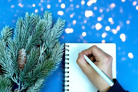 Mans right hand with pencil in white blank notebook writes plans and goals for next year on classic blue backgroung, the color of the year 2020. Bokeh style, Christmas concept.の写真素材