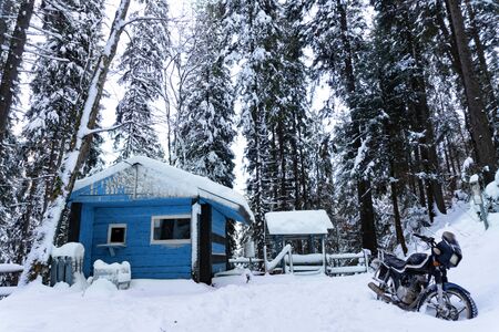 View at wooden buiding toned in classic blue in winter forest, motorcycle is on a side, snow is all around. Day time, good background. Winter forest concept.の写真素材