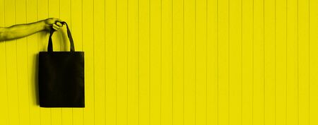Blank canvas dark black tote bag, design mockup with mans hand on yellow background. No plastic concept, minimal styleの写真素材